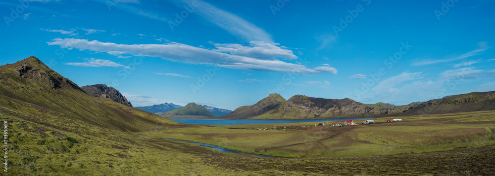 Panoramic landscape with mountain huts at camping site on blue Alftavatn lake with river, green hills and glacier in beautiful landscape of the Fjallabak Nature Reserve in the Highlands of Iceland