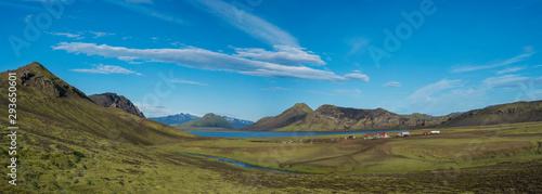 Panoramic landscape with mountain huts at camping site on blue Alftavatn lake with river, green hills and glacier in beautiful landscape of the Fjallabak Nature Reserve in the Highlands of Iceland