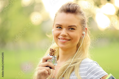 Fotografi Athletic woman eating a protein bar - Closeup portrait of smiling young sporty g
