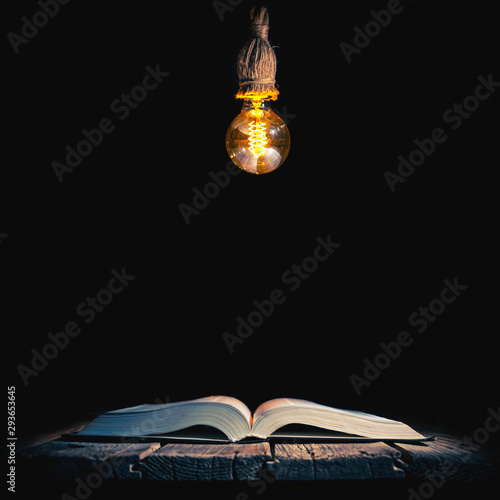 Old opened book and lamp hanging above isolated on black background