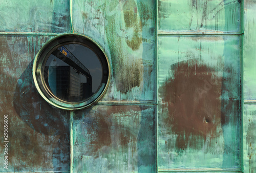 Vintage single round porthole window with reflection of a traffic sign. Green patina - natural oxidation of copper surface on sheets used for facade cladding. Control tower on Long bridge (Langebro).