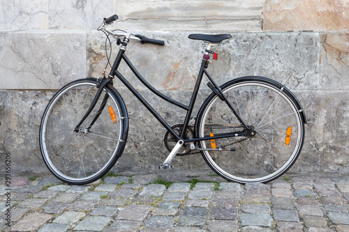 Plain black bike leaning against a marble wall in a cobblestone street.