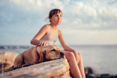 Girl embracing her dog while sitting on the rock by the sea