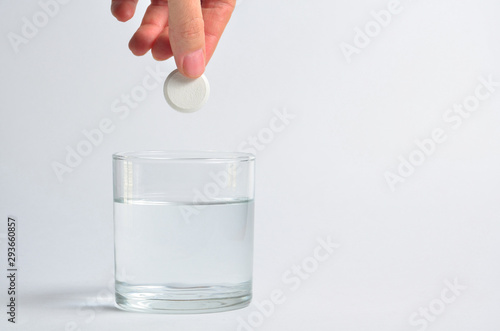 A hand holds an effervescent soluble tablet and places it in a glass of water. Isolated on white background. The concept of treatment of viral diseases. Help with depression and insomnia. Copy space
