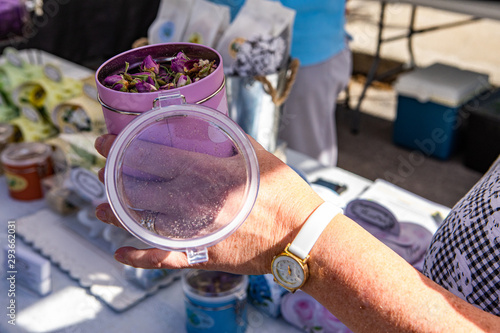Fresh food at outdoor farmer's market. Aromatic rose essence is seen in a pink tin, closeup in the hand of a trader selling homemade essential oils & perfumes during a local cottage industry fair
