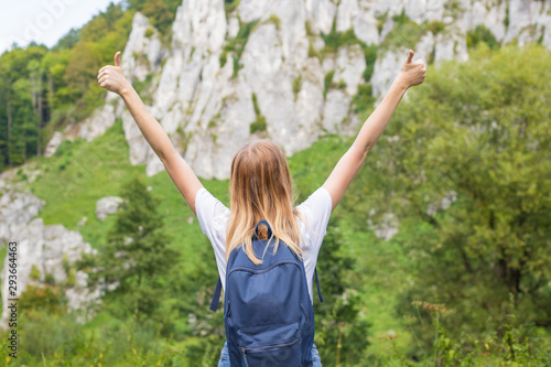 Young woman with backpack giving thumbs up. Trekking and tourism concept. Copyspace. A young pretty girl standing on a background of mountains
