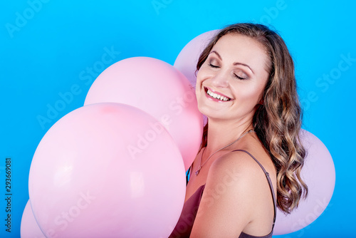 Happy smiling young woman with eyes closed holding pink air balloons over blue background. Holiday, birthday, valentine, fashion concept