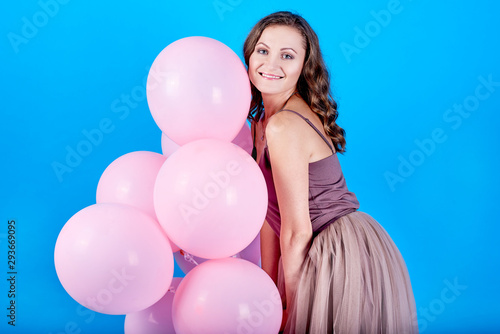 Happy young woman in dress holding pink air balloons over blue background. Holiday, birthday, valentine, fashion concept