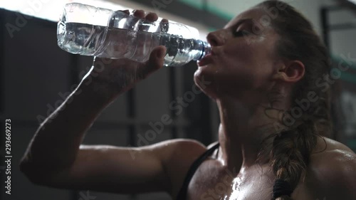  sporty beautiful woman eagerly drinking water from a bottle after training in the gym