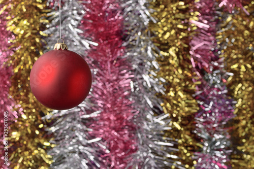 Red Christmas ball. Against the background of multicolored tinsel in blur.