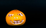 Mandarin isolated on a black background in the form of a halloween pumpkin. A terrible face is carved on the mandarin.