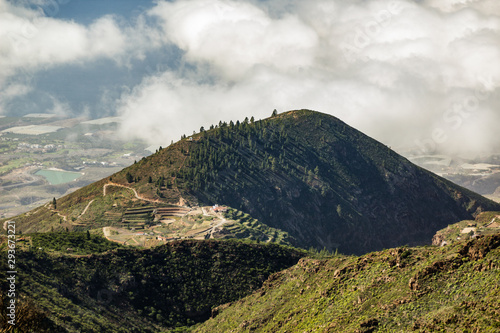 Aerial view of green mountains and southern coast of Tenerife from Macizo de Adeje. Warm sunny day and view point above beautiful white clouds. Long lens shot