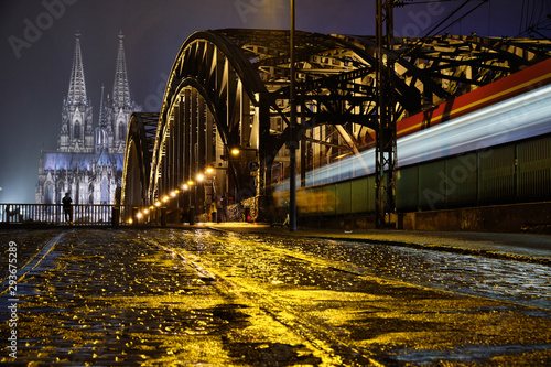 Kölner Dom Panorama mit Hohenzollernbrücke aus Bodenhöhe beim Regen und einem fahrendem Zug.
