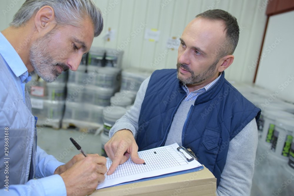 worker with cardboard box looking at male supervisor with clipboard