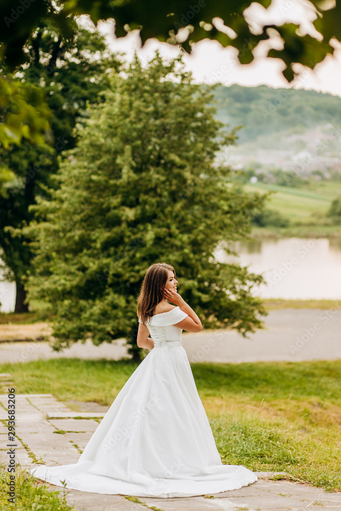 Bride in white dress standing with her back against the background of the lake Bride in white dress standing with her back against the background of the lake