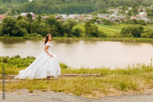 Pretty bride in white dress running near lake