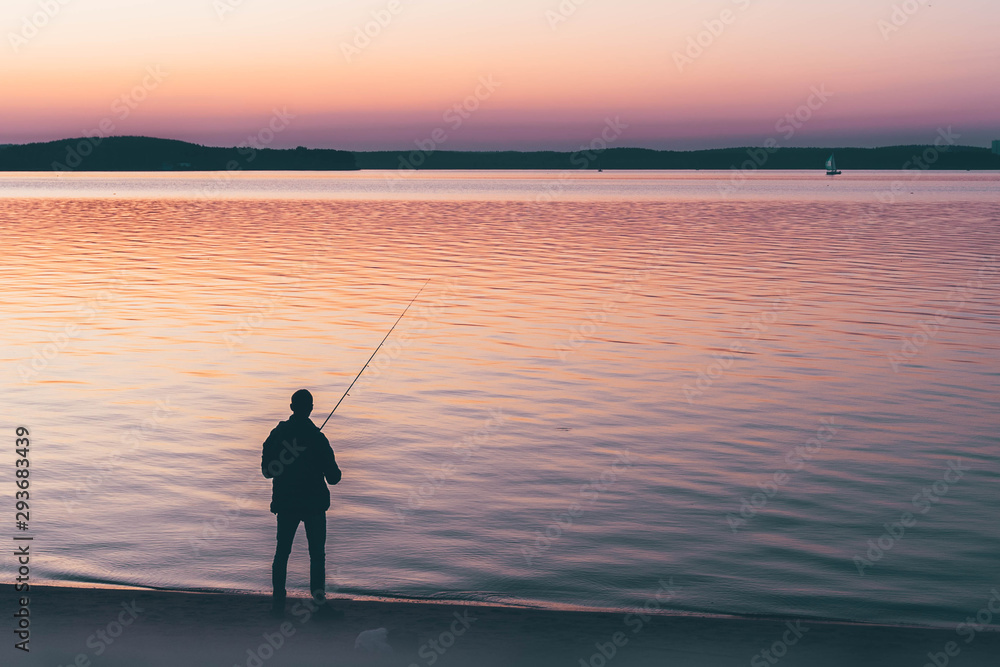 silhouette of fishermen satnding alone at a lake. yellow pink  orange sunset background.