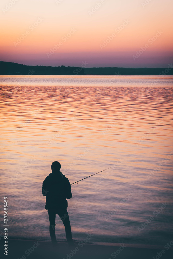 silhouette of fishermen satnding alone at a lake. yellow pink  orange sunset background.