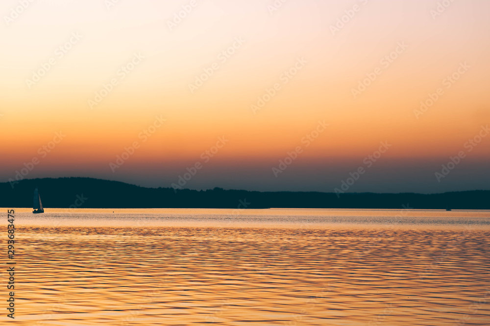 Sailing boats at sunset on background. many wild ducks swimming in water. silhouette of fishermen in a boat on a lake. Sailing boats at sunset on background. many wild ducks swimming in water. silhouette of fishermen in a boat on a lake.