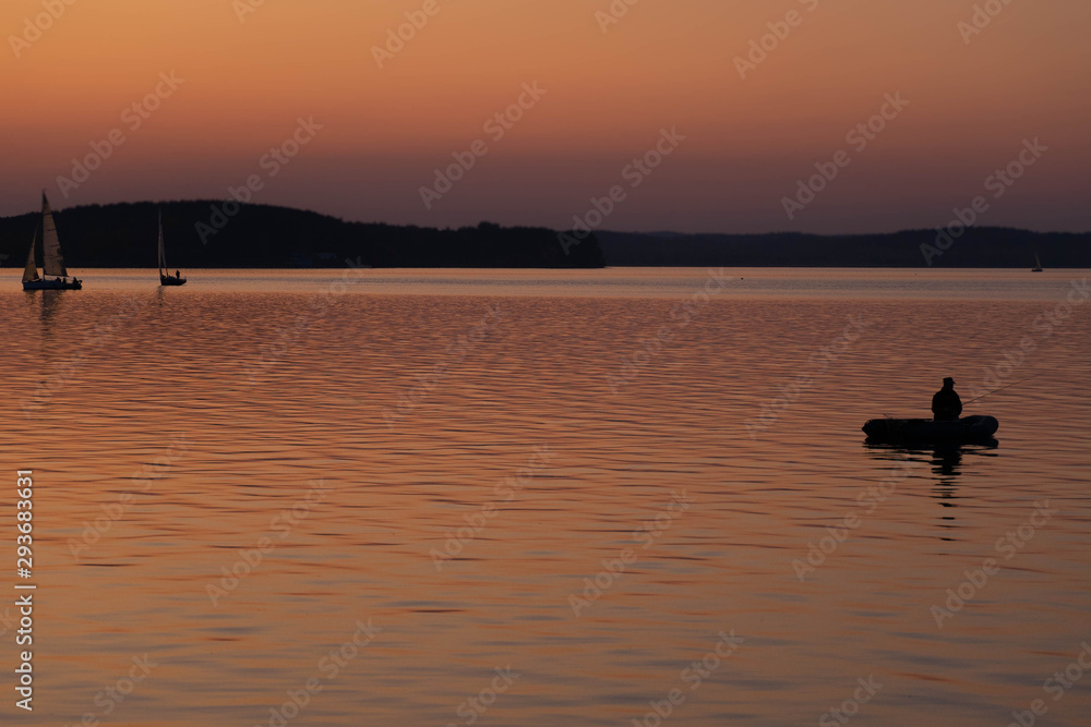 Fishing early in the morning. silhouette of fishermen in a boat on a lake. Sailing boats at sunset on background