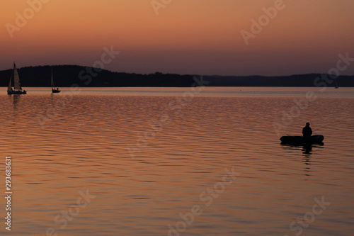 Fishing early in the morning. silhouette of fishermen in a boat on a lake. Sailing boats at sunset on background