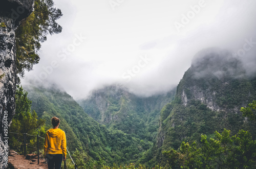 Young woman in yellow sweatshirt on a viewpoint in Levada Caldeirao Verde, Madeira, Portugal. Green scenic mountains in fog, misty landscape. Female traveler. Instagram, hipster filter