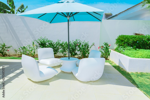 amazing relaxing inviting view of luxury outdoor backyard patio furniture with blue great umbrella and comfortable white beautiful chairs on sunny gorgeous summer day
