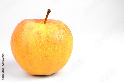 on a white background is highlighted a closeup of a yellow ripe apple with a ponytail and drops of water on the skin