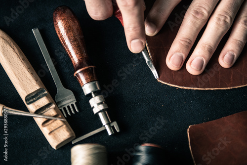 a young tanner on a desktop in a workshop chamfers a piece of brown leather with a special tool