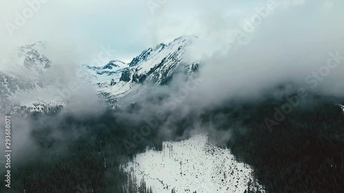Ascending slow aerial flight between snow covered mountains and clouds in winter. High Tatras, Slovakia and Poland. Shot was taken near to Strbske Pleso.