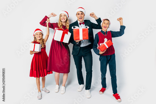 happy family Christmas with the kids in Santa hats, fun by showing the gesture of victory, holding Christmas gifts in hands on white background