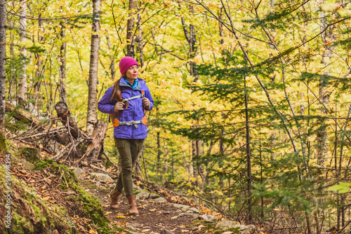 Autumn hike woman walking on forest trail with yellow leaves foliage. Fall outdoor Asian girl hiking with backpack.