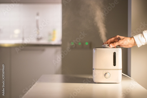 Billede på lærred Hand turn on aroma oil diffuser on the table at home, steam from the air humidifier, free space