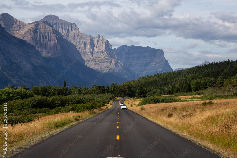 Beautiful View of Scenic Highway with American Rocky Mountain Landscape in the background during a Cloudy Summer Morning. Taken in Glacier National Park, Montana, United States. Beautiful View of Scenic Highway with American Rocky Mountain Landscape in the background during a Cloudy Summer Morning. Taken in Glacier National Park, Montana, United States.