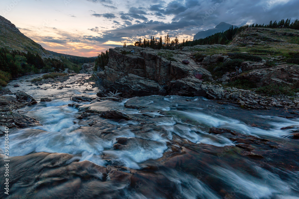 Fototapeta premium Beautiful View of the Glacier River during a cloudy morning sunrise in the American Rockies. Taken in Swiftcurrent Lake, Glacier National Park, Montana, United States.