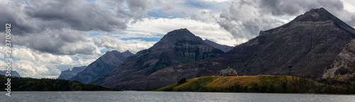 Iconic Hotel in Glacier Lake surrounded by the beautiful Canadian Rocky Mountains during a cloudy summer sunset. Taken in Upper Waterton Lake, Alberta, Canada.