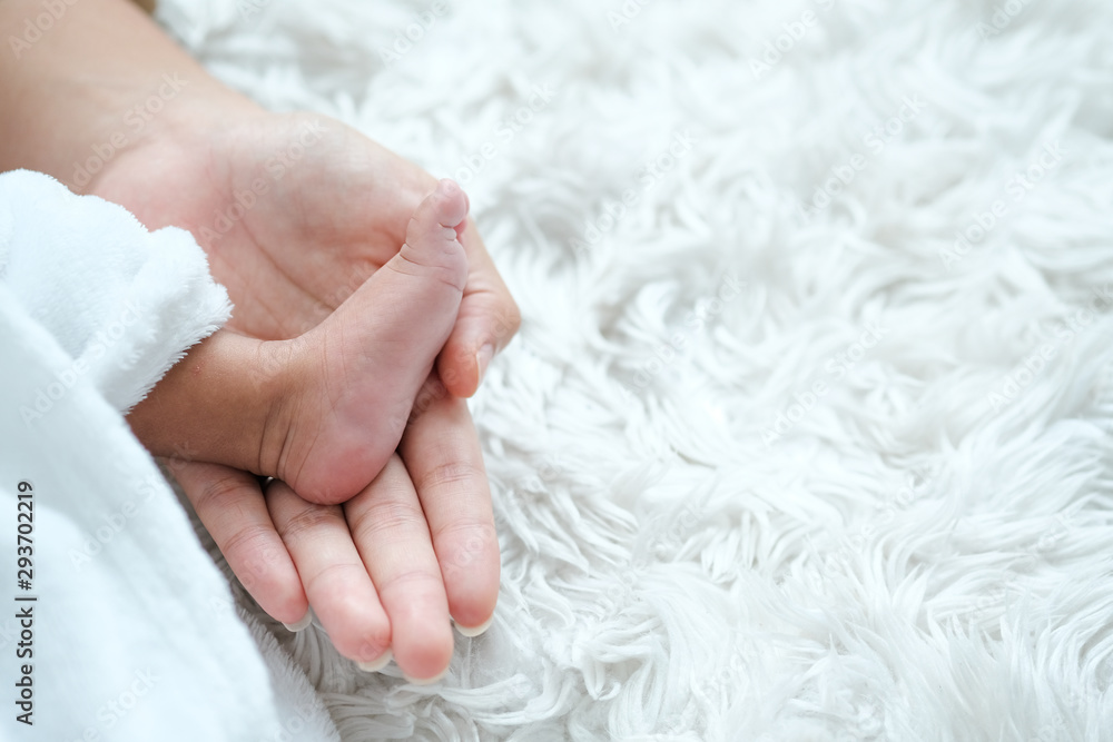 One foot of newborn baby is put on her mother hand on white bed with day light. One foot of newborn baby is put on her mother hand on white bed with day light.