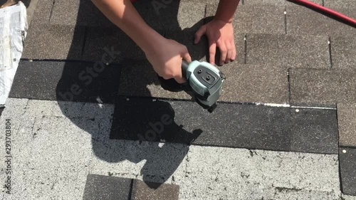 Nail fun in slow motion from above as roofer affixes shingles over existing roof. 