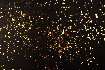 Gold foil confetti on black background. Flatlay.