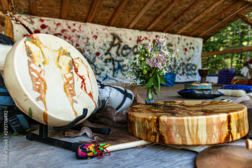 Diverse people enjoy spiritual gathering Traditional rawhide native drums and sacred objects are viewed close up at a sacred site in nature, with beater, colorful cushions and flowers. photo