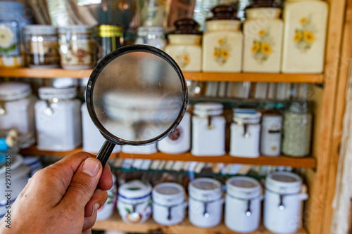 Indoor damp & air quality (IAQ) testing. Looking for signs of damp and mold inside the kitchen pantry with a magnifying glass, blurred storage jars are seen displayed on vintage wooden shelves.