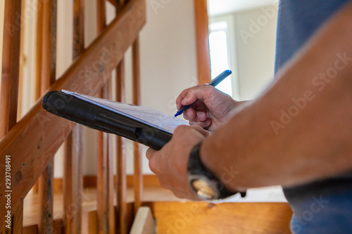 Indoor damp & air quality (IAQ) testing. A close up view on the hands of a professional building inspector, standing near a staircase filling in forms on overall environmental quality indoors. photo