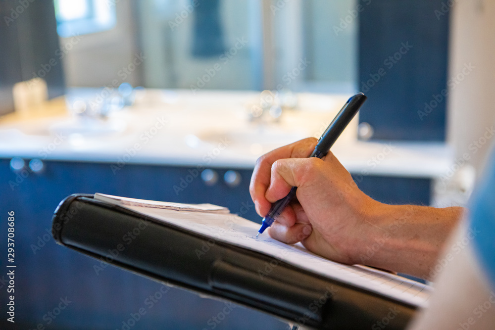 Obraz premium Indoor damp & air quality (IAQ) testing. An extreme close-up view on the hand of a man using a blue pen to take handwritten notes during an indoor building inspection, with room for copy.