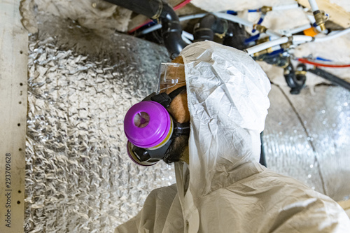 Indoor damp & air quality (IAQ) testing. A close up and side profile view of a domestic building surveyor at work, wearing respirator, white boiler suit and protective glasses during an assessment. photo