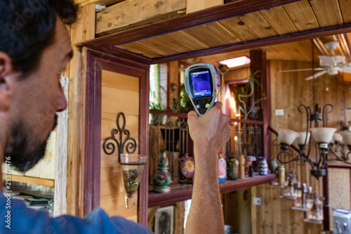 Indoor damp & air quality (IAQ) testing. A close up and side view of a professional indoor environmental quality (IEQ) assessor at work, using an infrared thermovision device to check for cold spots. photo