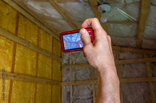 Indoor damp & air quality (IAQ) testing. A close up view of an indoor environmental quality home inspector using a small digital camera to photograph insulated walls and ceiling in domestic property. photo