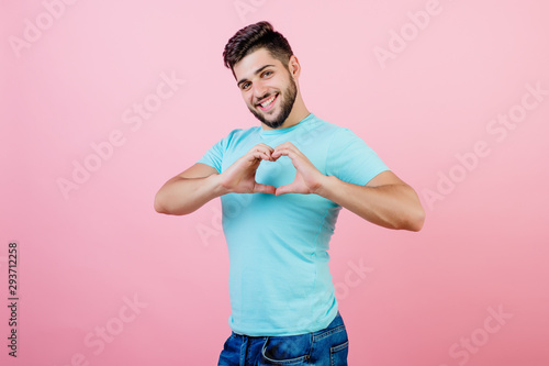 handsome smiling bearded guy showing heart with hands isolated over pink
