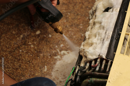 Wash away foam from air conditioner with high pressure water sprayer. Air conditioner maintenance, repair & service concept.
