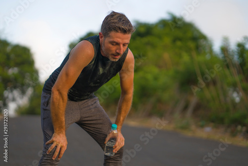 sport and fitness lifestyle portrait of young attractive sweaty and tired man exhausted after outdoors running workout on beautiful country road breathing