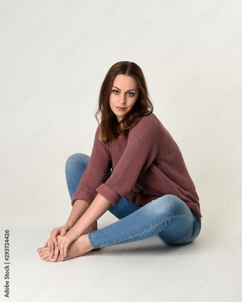 full length portrait of brunette woman wearing jeans and pink jumper. seated pose with a white studio background. full length portrait of brunette woman wearing jeans and pink jumper. seated pose with a white studio background.